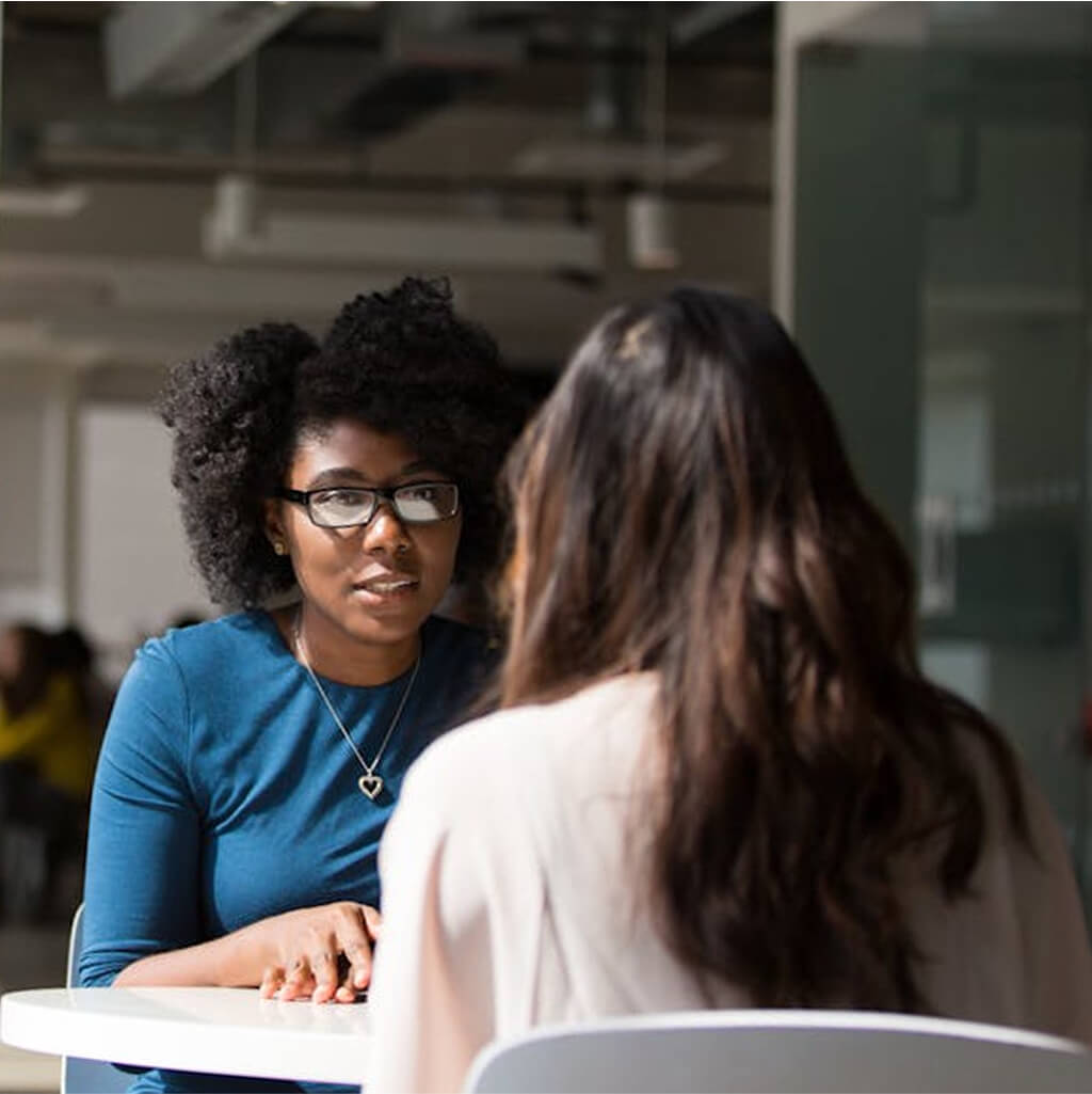 Deux femmes sont assises l'une en face de l'autre à une table dans un bureau et discutent de l'art-thérapie.