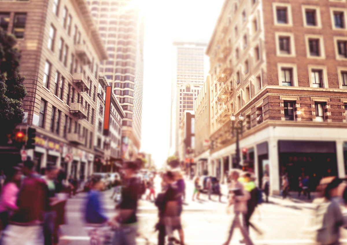 Una concurrida calle de la ciudad con peatones borrosos cruzando en una intersección entre edificios altos a la luz del día.